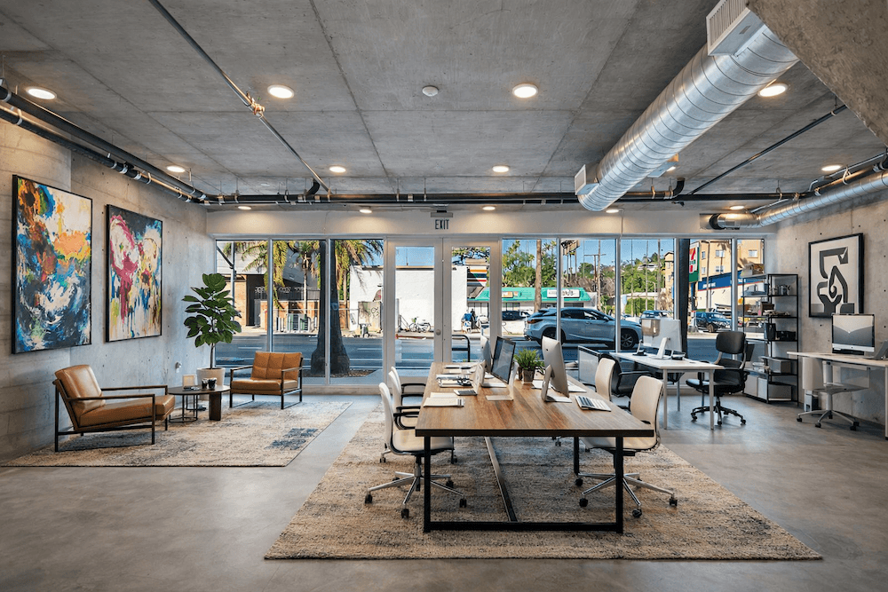 Fusion Hollywood live/work staged apartment with a large desk in the center with white chairs and concrete walls and floors